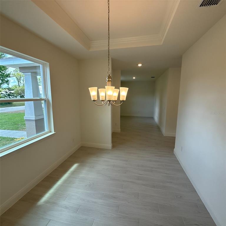 A dining area features a tray ceiling, a chandelier, and light-colored wood-look tile flooring — 106 FORRESTER PLACE, PALM COAST, FL