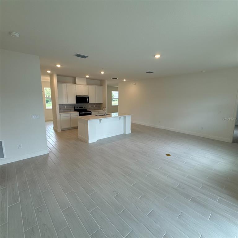 An open-concept kitchen features white cabinetry, a central island, and light-colored wood-look tile flooring — 106 FORRESTER PLACE, PALM COAST, FL