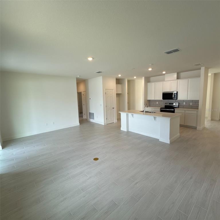 An open-concept kitchen and living area features light wood-look tile flooring and white cabinetry — 106 FORRESTER PLACE, PALM COAST, FL