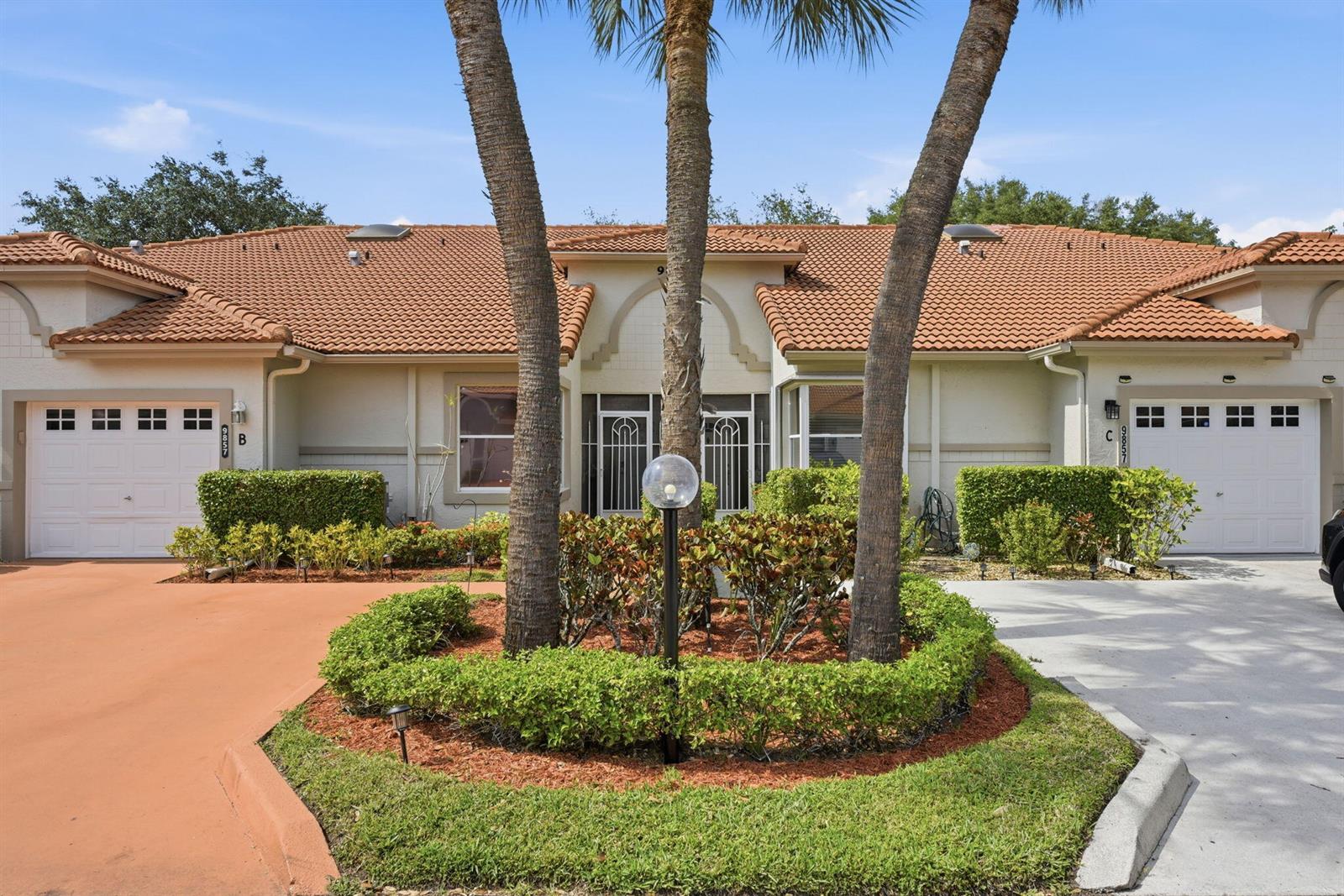 A duplex home features a shared central entrance, palm trees, and two separate garage doors — 9857 Summerbrook Terrace # B, Boynton Beach FL 33437, BOYNTON BEACH, FL