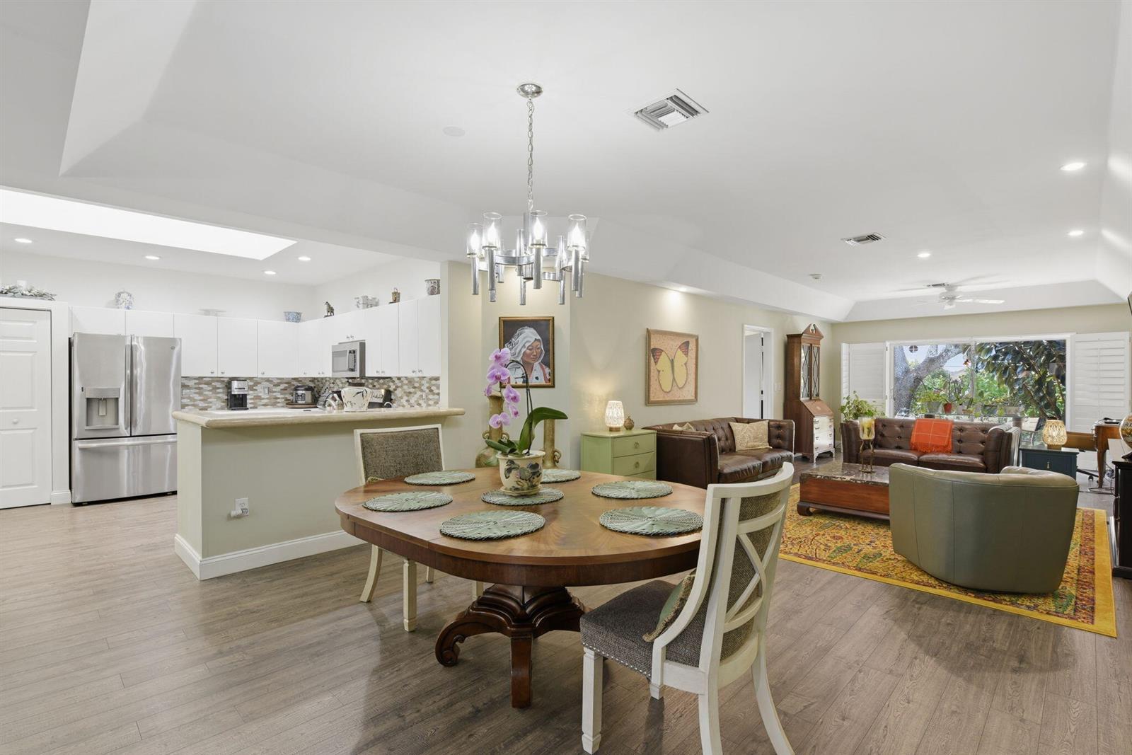 An open-concept living and dining area features a round wooden table, kitchen, and leather furniture — 9857 Summerbrook Terrace # B, Boynton Beach FL 33437, BOYNTON BEACH, FL