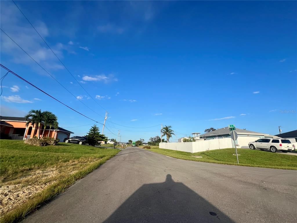 A paved residential street leads toward houses under a clear blue sky — 614 NE 12TH STREET, CAPE CORAL, FL
