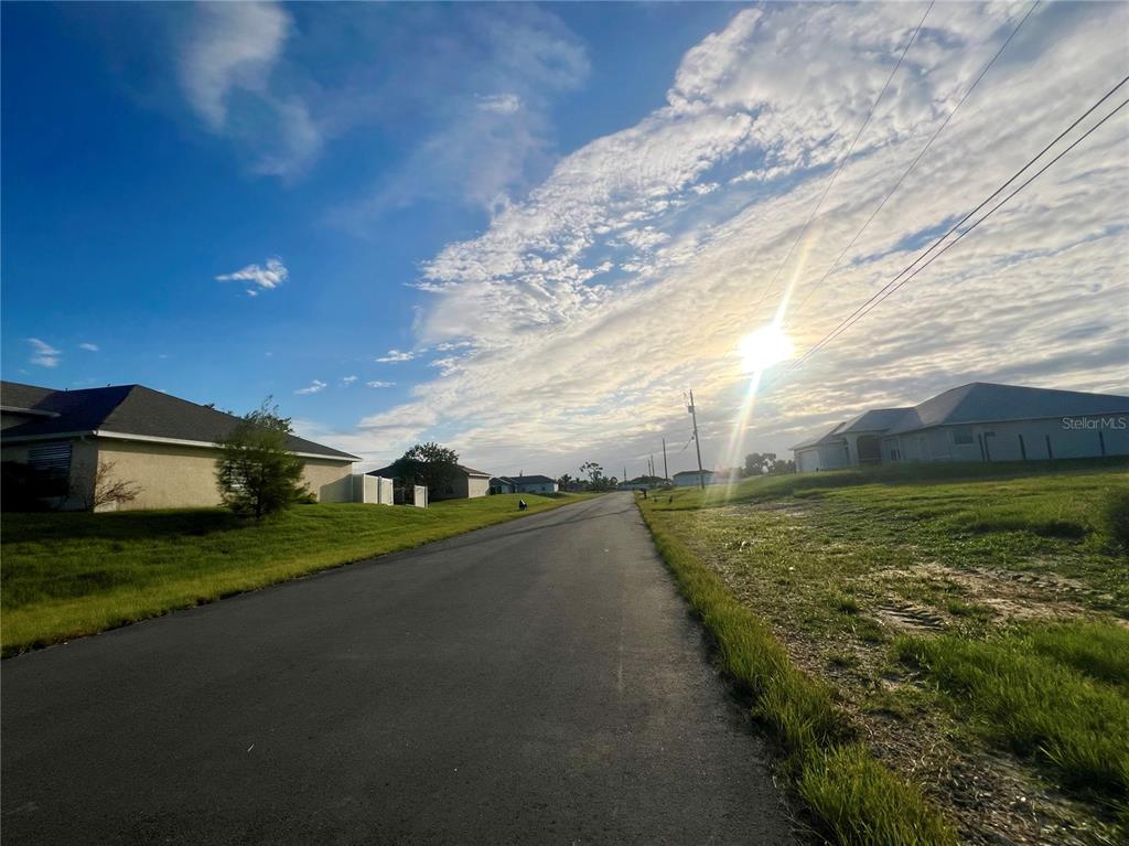 A paved residential street stretches toward the horizon under a bright, sunny sky — 614 NE 12TH STREET, CAPE CORAL, FL