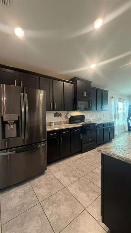 A kitchen features dark cabinetry, stainless steel appliances, granite countertops, and light-colored tile flooring — 365 CITRUS POINTE DRIVE, DAVENPORT, FL