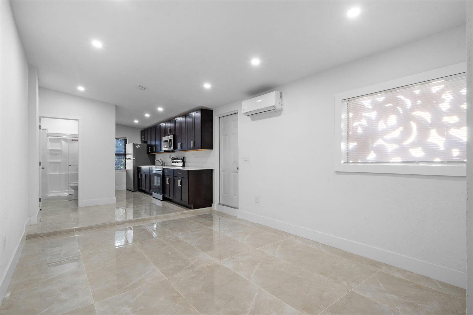 A kitchen and living area with white walls, dark cabinets, and light-colored tile flooring — 1300 NW 90th Street, Miami FL 33147, MIAMI, FL