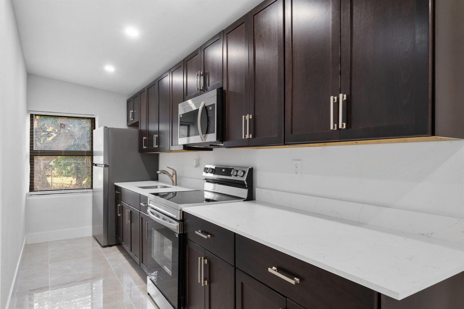 A galley kitchen features dark wood cabinets, white quartz countertops, and stainless steel appliances — 1300 NW 90th Street, Miami FL 33147, MIAMI, FL
