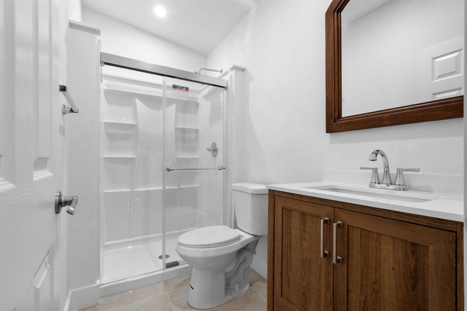 A bathroom features a glass-enclosed shower, a white toilet, and a wood vanity with sink — 1300 NW 90th Street, Miami FL 33147, MIAMI, FL