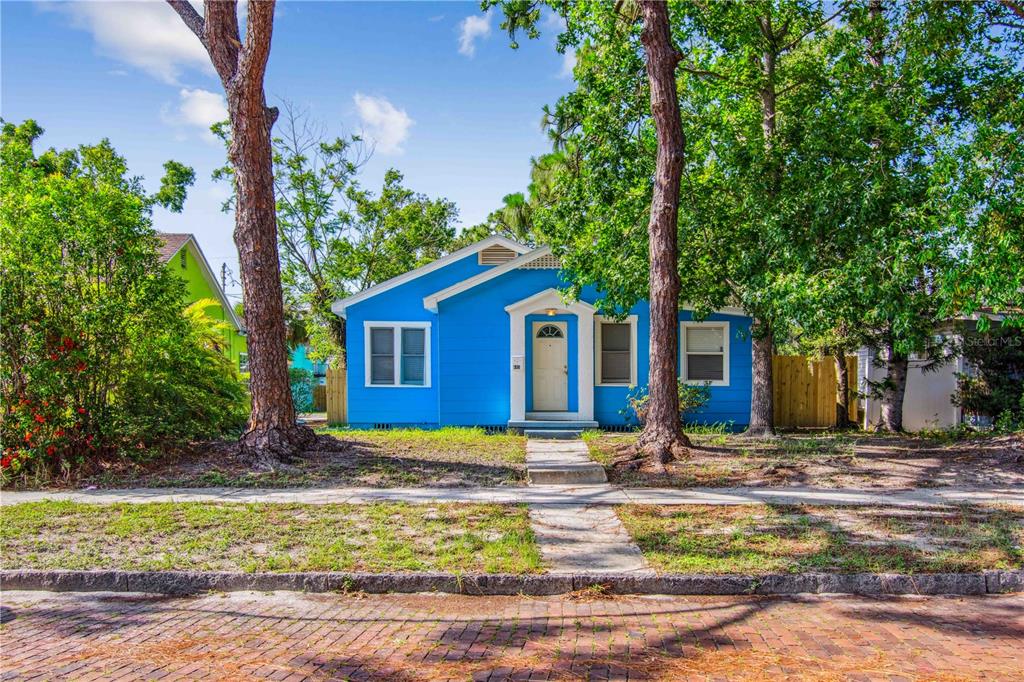 A bright blue single-story house stands behind a brick street and mature trees — 4411 3RD AVENUE S, ST PETERSBURG, FL