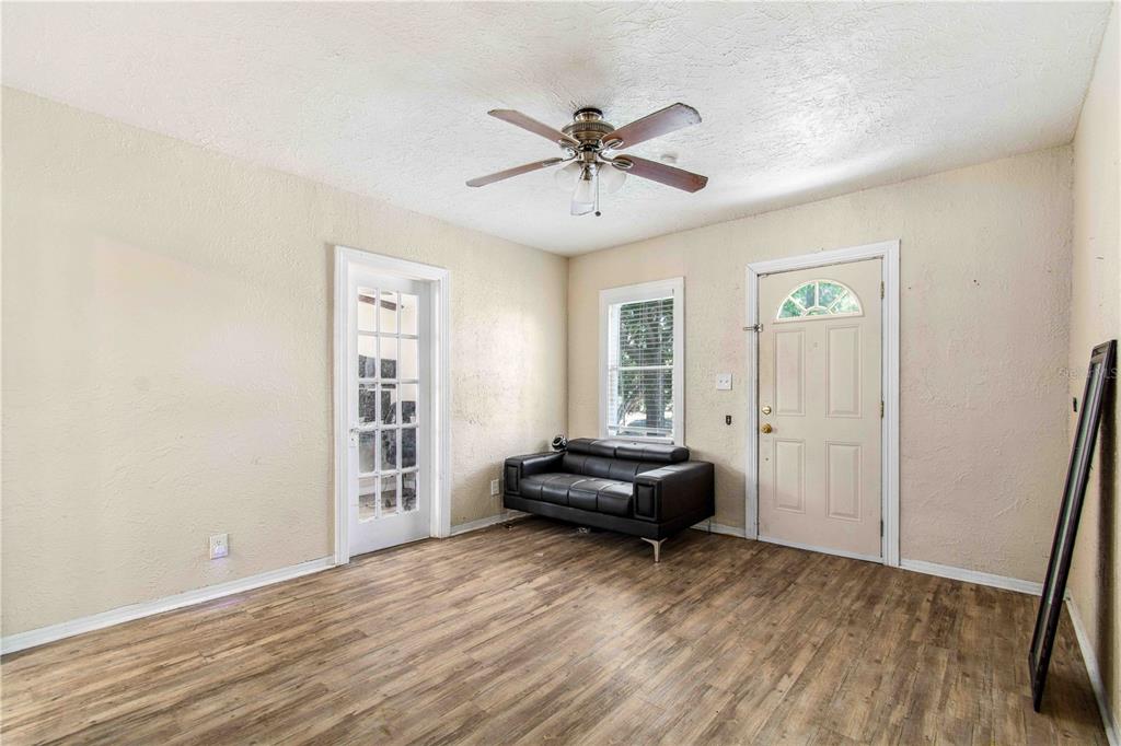 A room with wood-look flooring, a black sofa, a ceiling fan, and two doors — 4411 3RD AVENUE S, ST PETERSBURG, FL