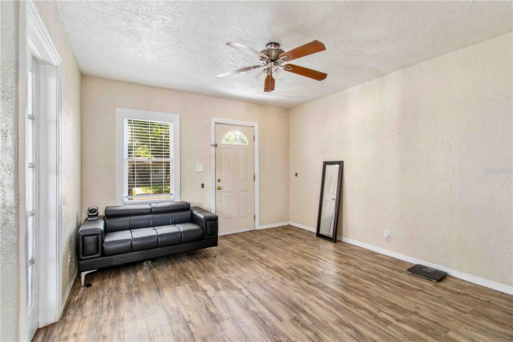A room with wood-look flooring, a black sofa, a ceiling fan, and a front door — 4411 3RD AVENUE S, ST PETERSBURG, FL