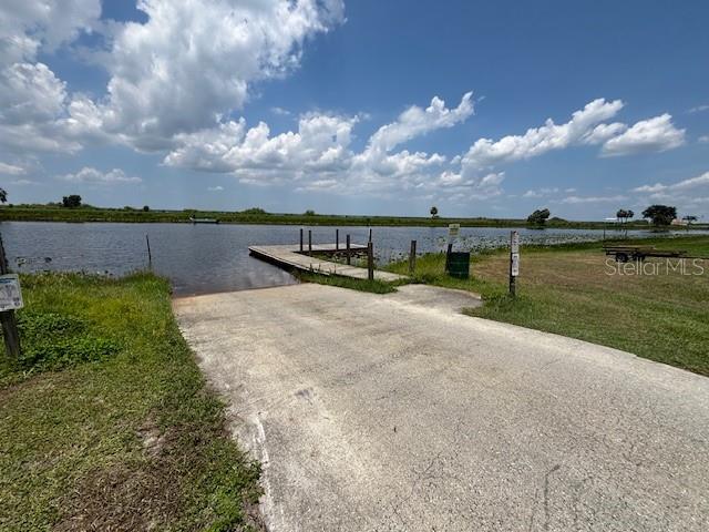 A concrete boat ramp leads to a wooden dock on a lake under a cloudy sky — 3371 AZALEA DRIVE, INDIAN LAKE ESTATES, FL