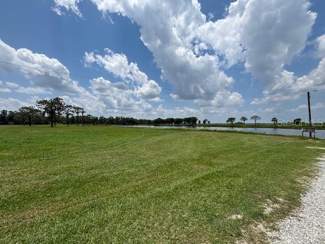 A large, grassy field leads to a pond under a cloudy blue sky — 3371 AZALEA DRIVE, INDIAN LAKE ESTATES, FL