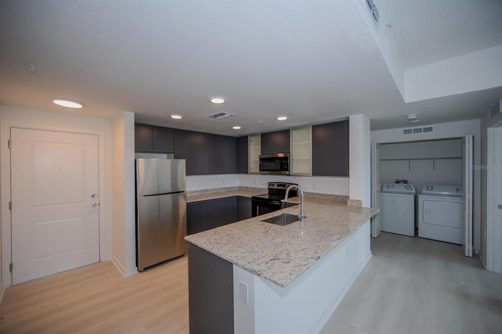 A kitchen features dark cabinets, granite countertops, stainless steel appliances, and an adjacent laundry closet — 5579 MILLENIA PARK BLVD UNIT 209, ORLANDO, FL