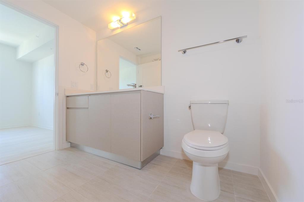 A bathroom features a light-colored vanity with a mirror, a toilet, and tile flooring — 5579 MILLENIA PARK BLVD UNIT 209, ORLANDO, FL