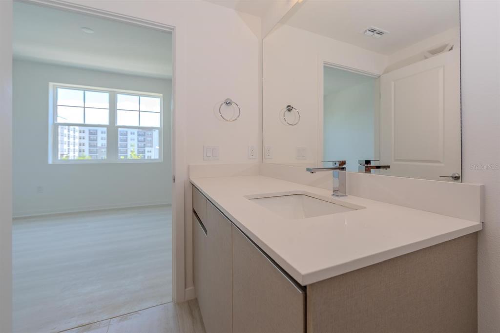 A modern bathroom vanity with a white countertop and sink sits beside a bedroom doorway — 5579 MILLENIA PARK BLVD UNIT 209, ORLANDO, FL