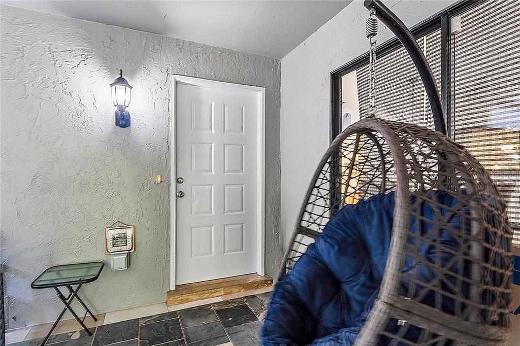 A covered patio features a white door, a hanging wicker chair, and slate tile flooring — 12742 WOOD TRAIL BLVD BOULEVARD, TAMPA, FL