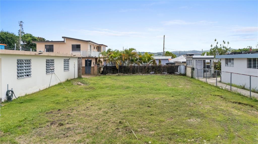 A grassy vacant lot is situated between two residential buildings with a chain-link fence — CII JOSE CAMPECHE, LAS PIEDRAS, PR