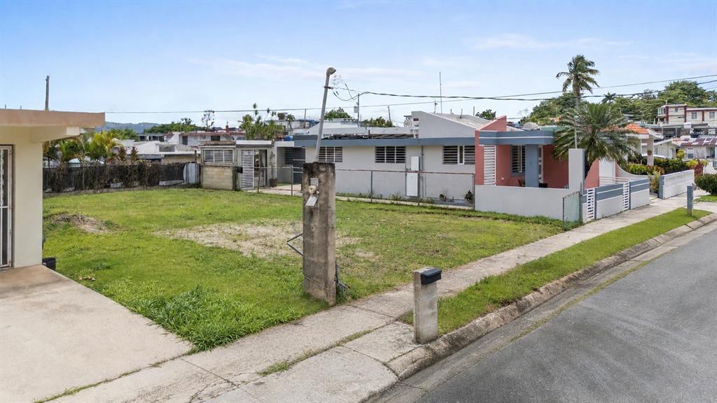 A vacant residential lot sits between two houses along a paved street with a sidewalk — CII JOSE CAMPECHE, LAS PIEDRAS, PR