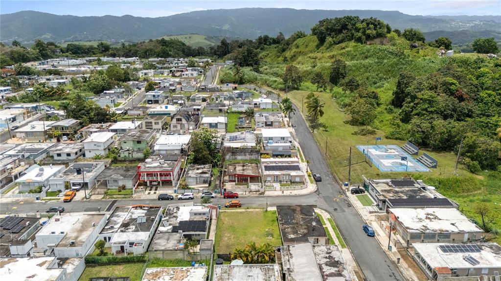 An aerial view shows a residential neighborhood with houses, a basketball court, and nearby hills — CII JOSE CAMPECHE, LAS PIEDRAS, PR