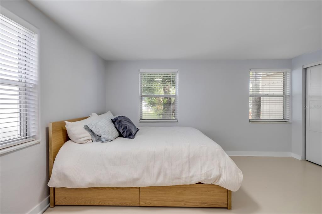A bedroom features light gray walls, a wooden platform bed, and three windows with blinds — 308 DUE EAST STREET, NEW SMYRNA BEACH, FL