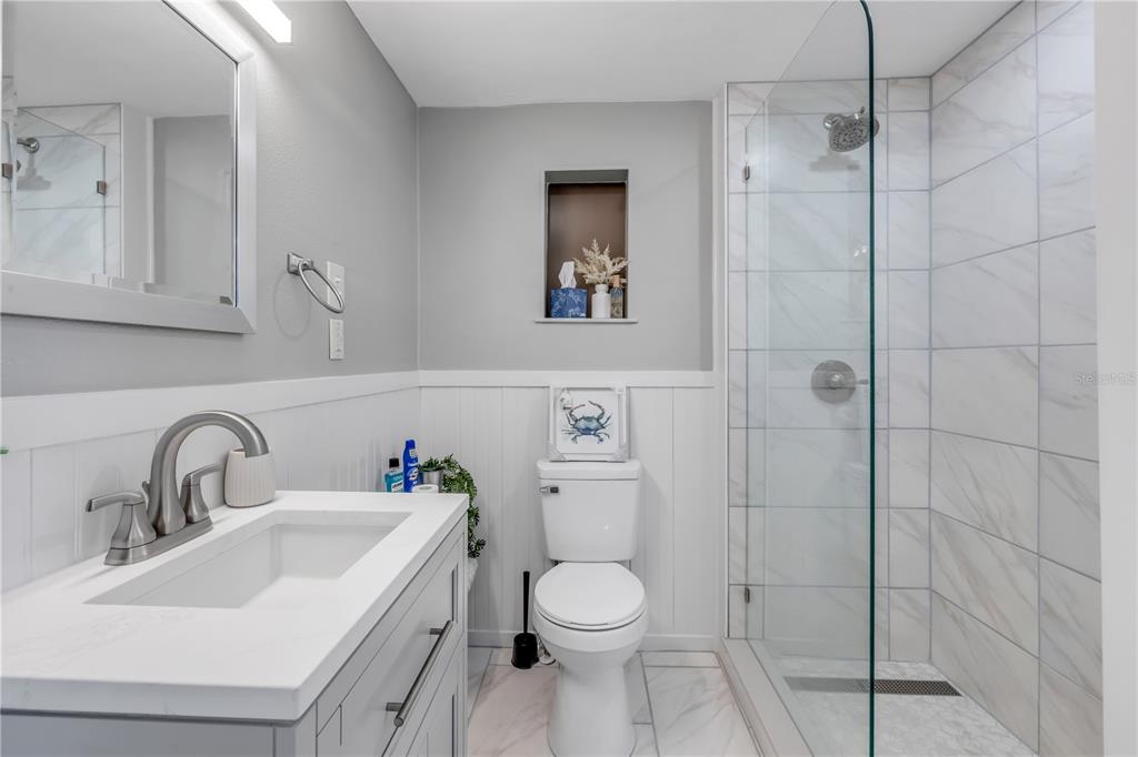 A bathroom features a white vanity, a toilet, and a glass-enclosed walk-in shower with tile — 308 DUE EAST STREET, NEW SMYRNA BEACH, FL