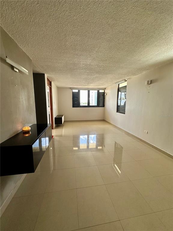 A spacious, empty living room features glossy light-colored tile floors, a textured ceiling, and windows — 171 CALLE SAN JORGE UNIT Ph702, SAN JUAN, PR