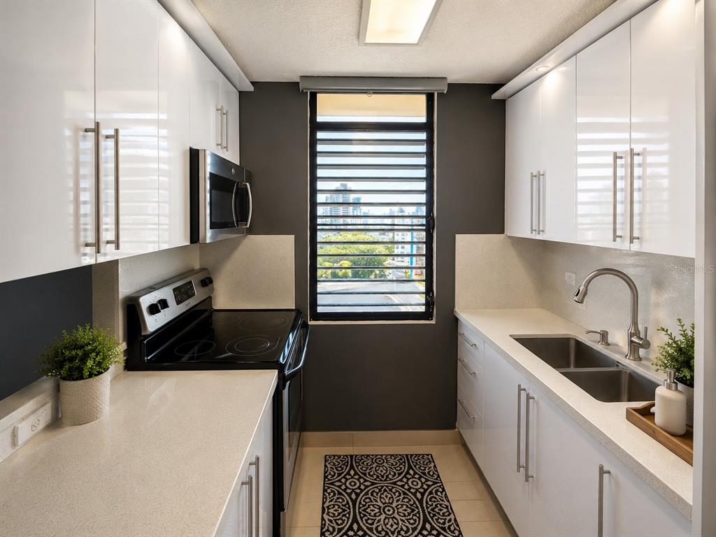A galley kitchen features white cabinets, quartz countertops, stainless steel appliances, and a window view — 171 CALLE SAN JORGE UNIT Ph702, SAN JUAN, PR