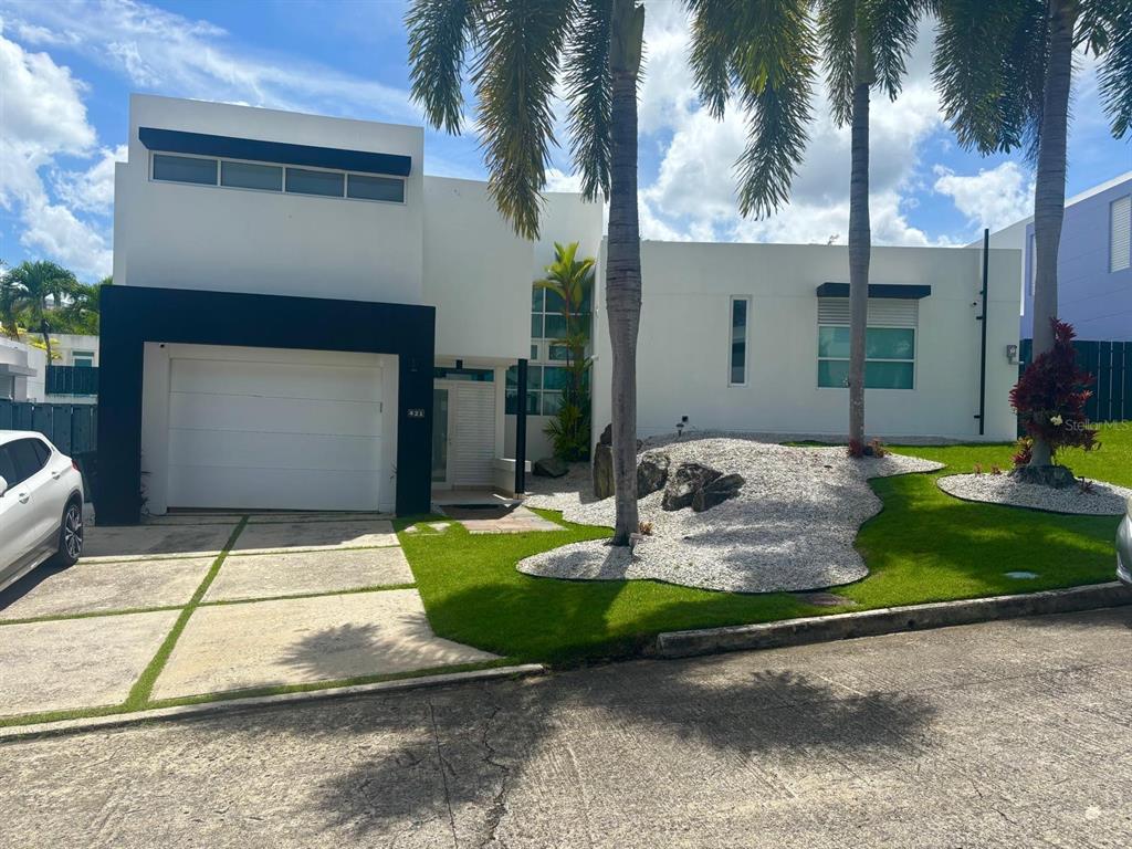 A modern white house with a black garage frame, palm trees, and a landscaped yard — C LERIDA, CAGUAS, PR