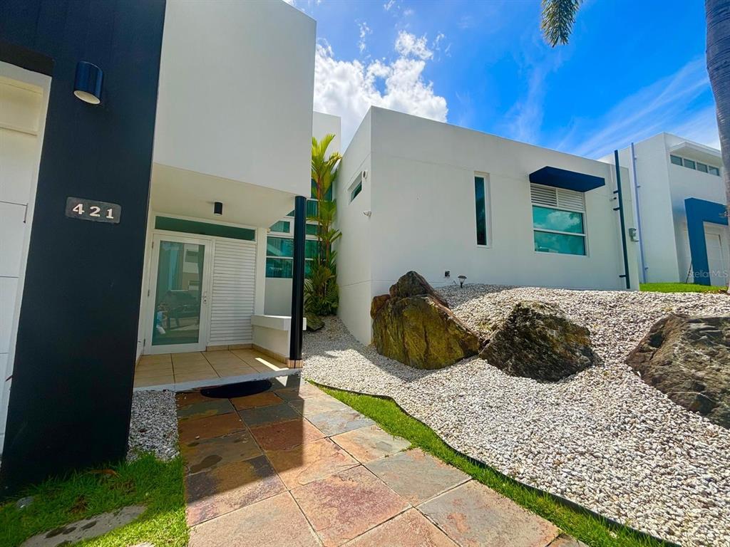 A modern white house exterior features a stone walkway, large boulders, and a glass door — C LERIDA, CAGUAS, PR