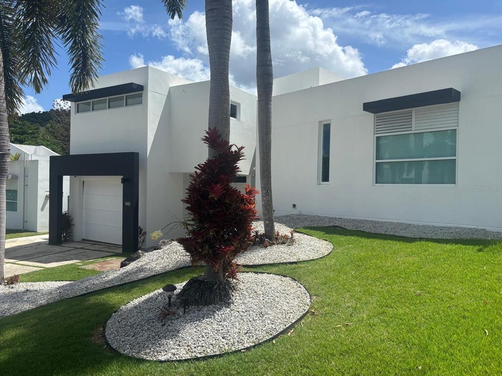 A modern white house with a black garage frame, palm trees, and landscaped gravel beds — C LERIDA, CAGUAS, PR