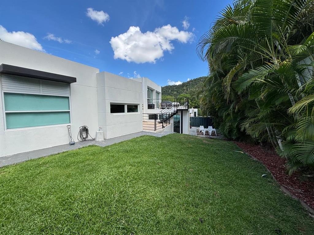 A white modern house exterior features a grassy backyard, a metal staircase, and palm trees — C LERIDA, CAGUAS, PR