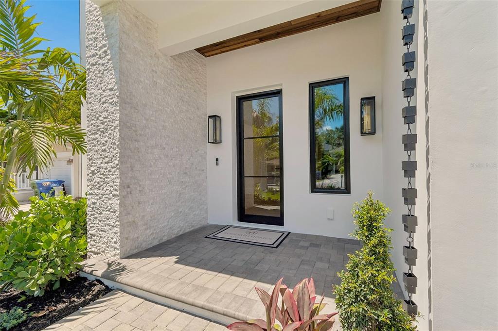 A modern home entrance features a stone-clad wall, a glass-paned door, and a paver porch — 3605 W KENSINGTON AVENUE, TAMPA, FL