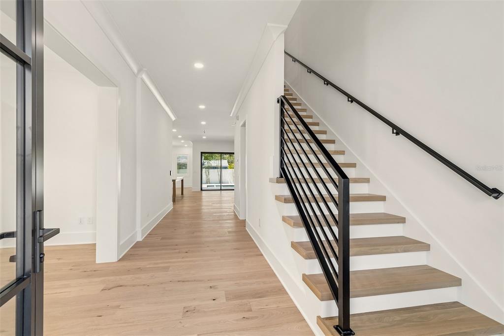 A bright hallway features light wood flooring, white walls, and a staircase with black railings — 3605 W KENSINGTON AVENUE, TAMPA, FL