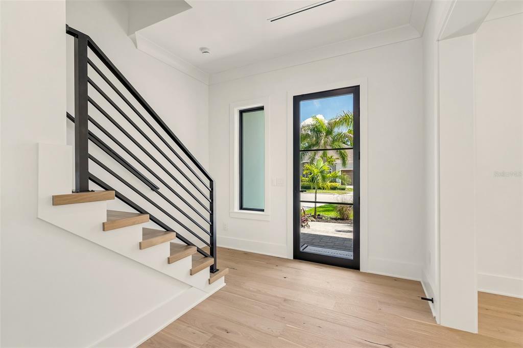 A modern entryway features light wood flooring, a black metal staircase railing, and a glass door — 3605 W KENSINGTON AVENUE, TAMPA, FL