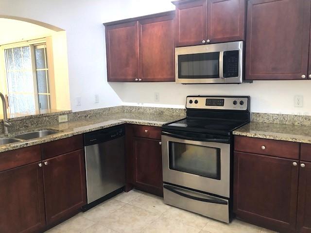 A kitchen features dark wood cabinets, granite countertops, and stainless steel appliances — 102 VISTA VERDI CIRCLE UNIT 112, LAKE MARY, FL