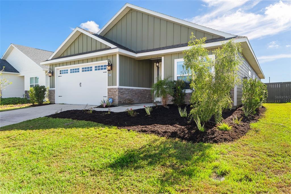 A single-story house with olive green vertical siding, a stone base, and a two-car garage — 1689 SW 71ST CIRCLE, GAINESVILLE, FL