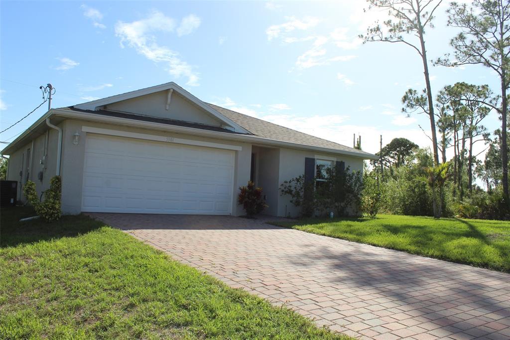 A single-story house with a white garage door and a paved driveway under a blue sky — 5501 KEMPSON LANE, PORT CHARLOTTE, FL