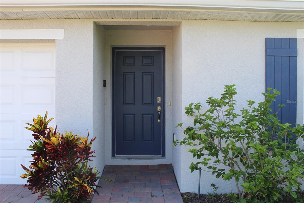 A blue front door is set in a recessed entryway next to a garage — 5501 KEMPSON LANE, PORT CHARLOTTE, FL