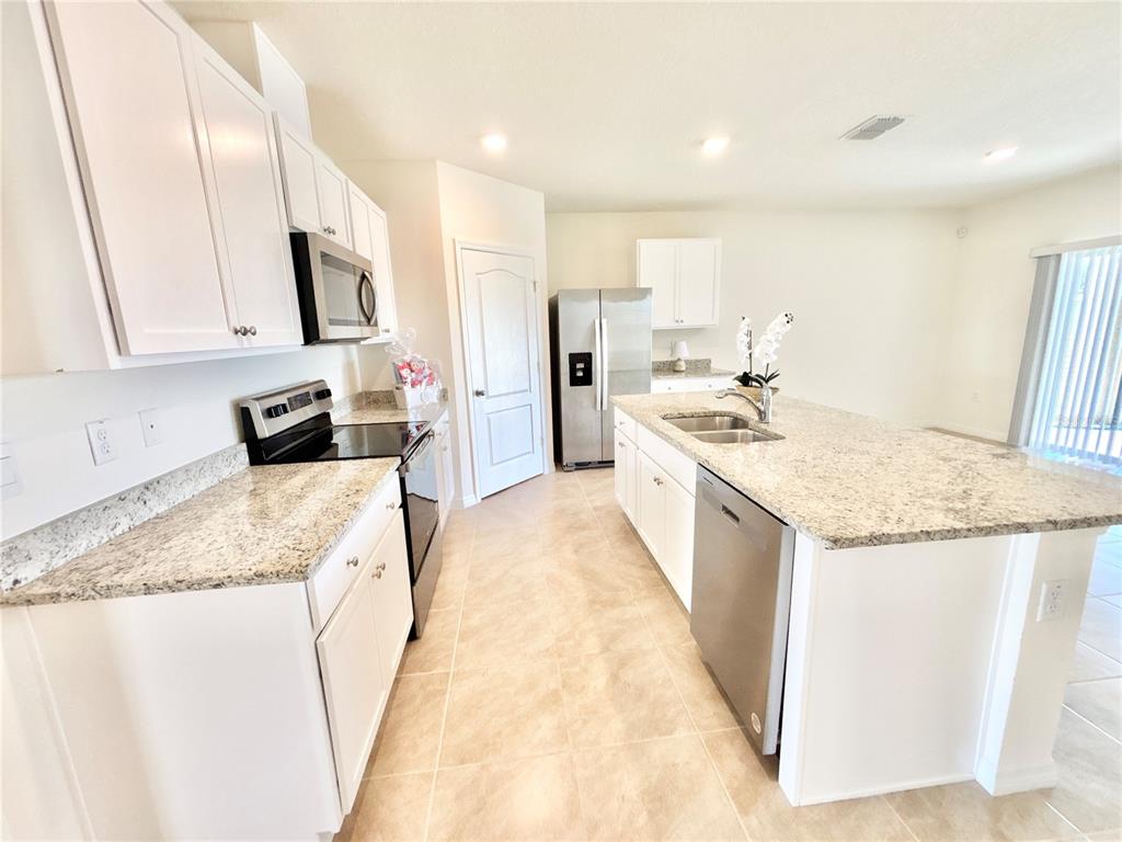 A kitchen features white cabinetry, granite countertops, stainless steel appliances, and tile flooring — 2752 GENTLE RAIN DRIVE, DAVENPORT, FL