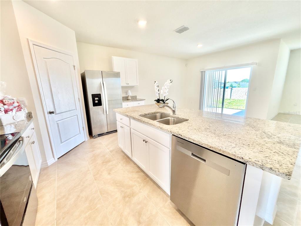 A kitchen features white cabinets, granite countertops, stainless steel appliances, and tile flooring — 2752 GENTLE RAIN DRIVE, DAVENPORT, FL