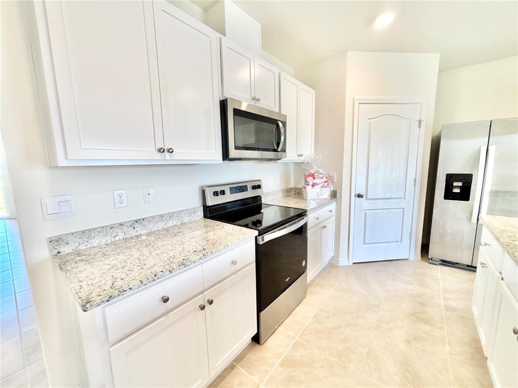 A kitchen features white cabinets, granite countertops, stainless steel appliances, and light tile flooring — 2752 GENTLE RAIN DRIVE, DAVENPORT, FL