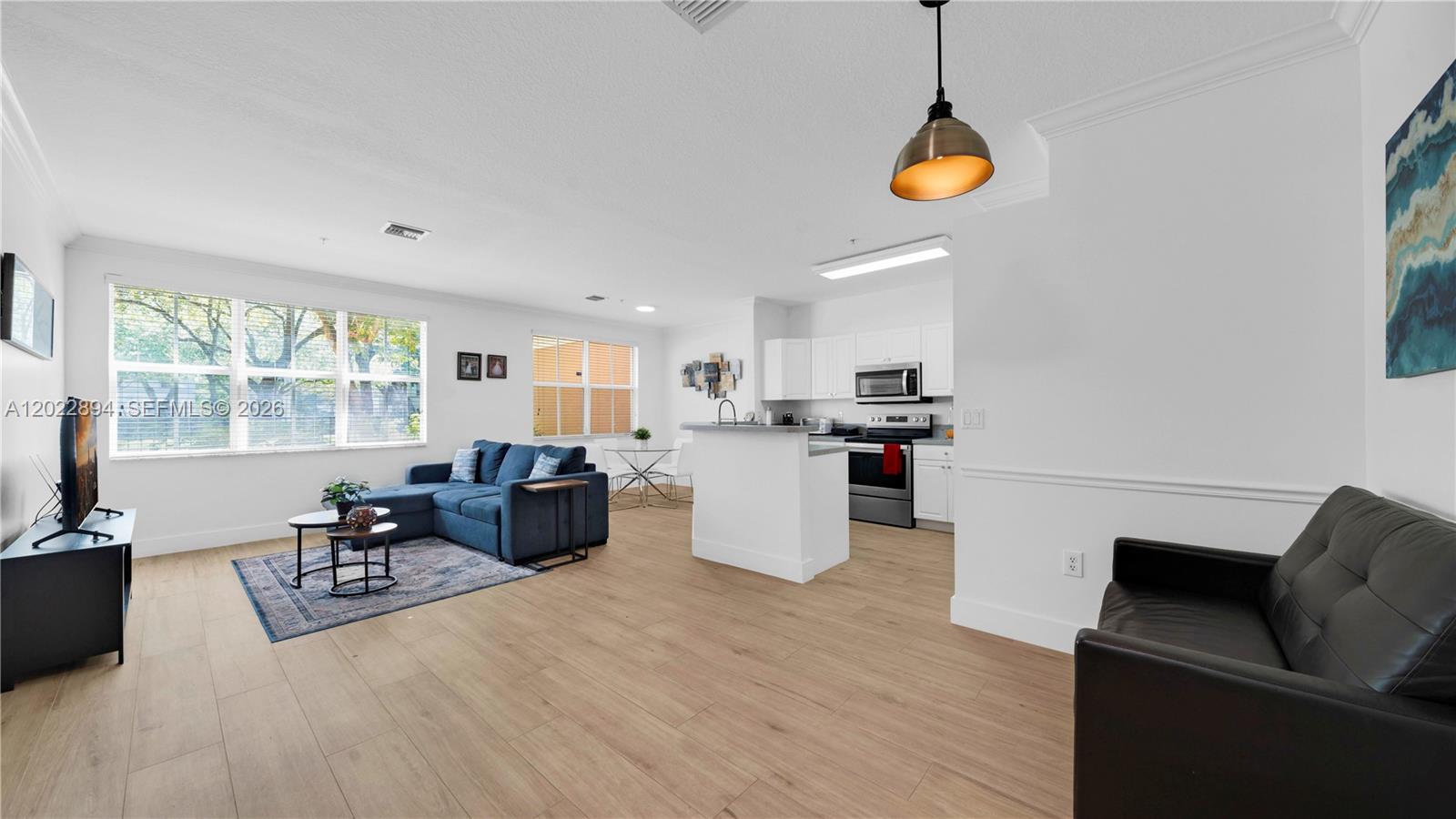 An open-concept living area features light wood flooring, a kitchen with white cabinets, and furniture — 4400 SW 160th Ave # 1015, Miramar FL 33027, MIRAMAR, FL