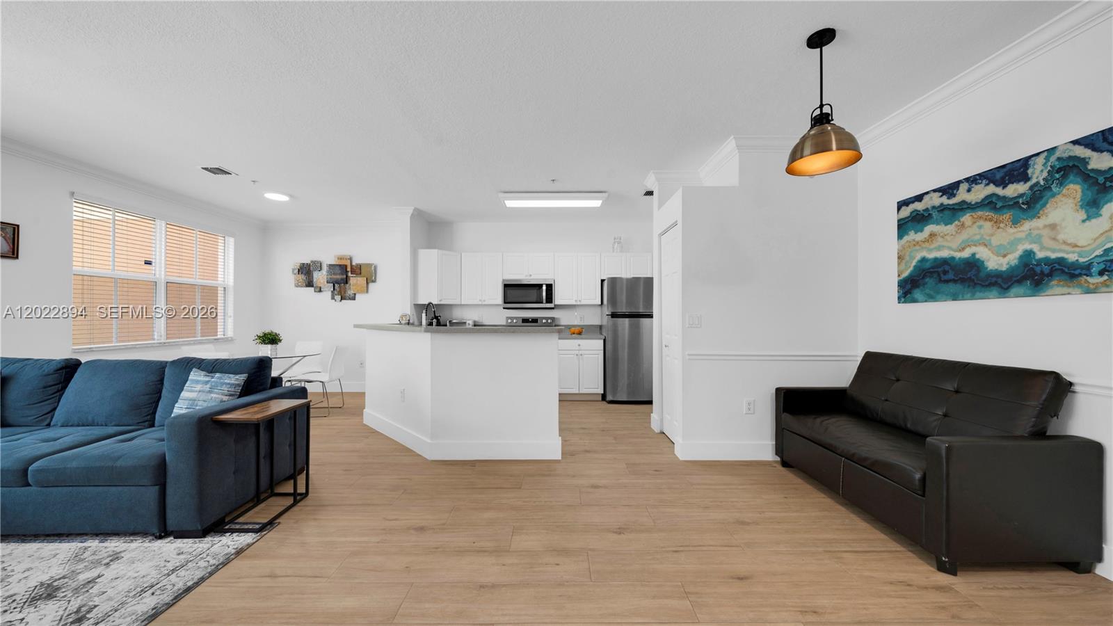 This open-concept living area features a kitchen with white cabinetry and light wood flooring — 4400 SW 160th Ave # 1015, Miramar FL 33027, MIRAMAR, FL