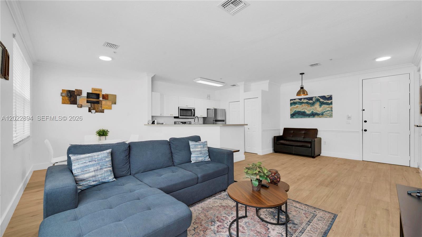 A living room with a blue sectional sofa, wood-look flooring, and an open kitchen area — 4400 SW 160th Ave # 1015, Miramar FL 33027, MIRAMAR, FL