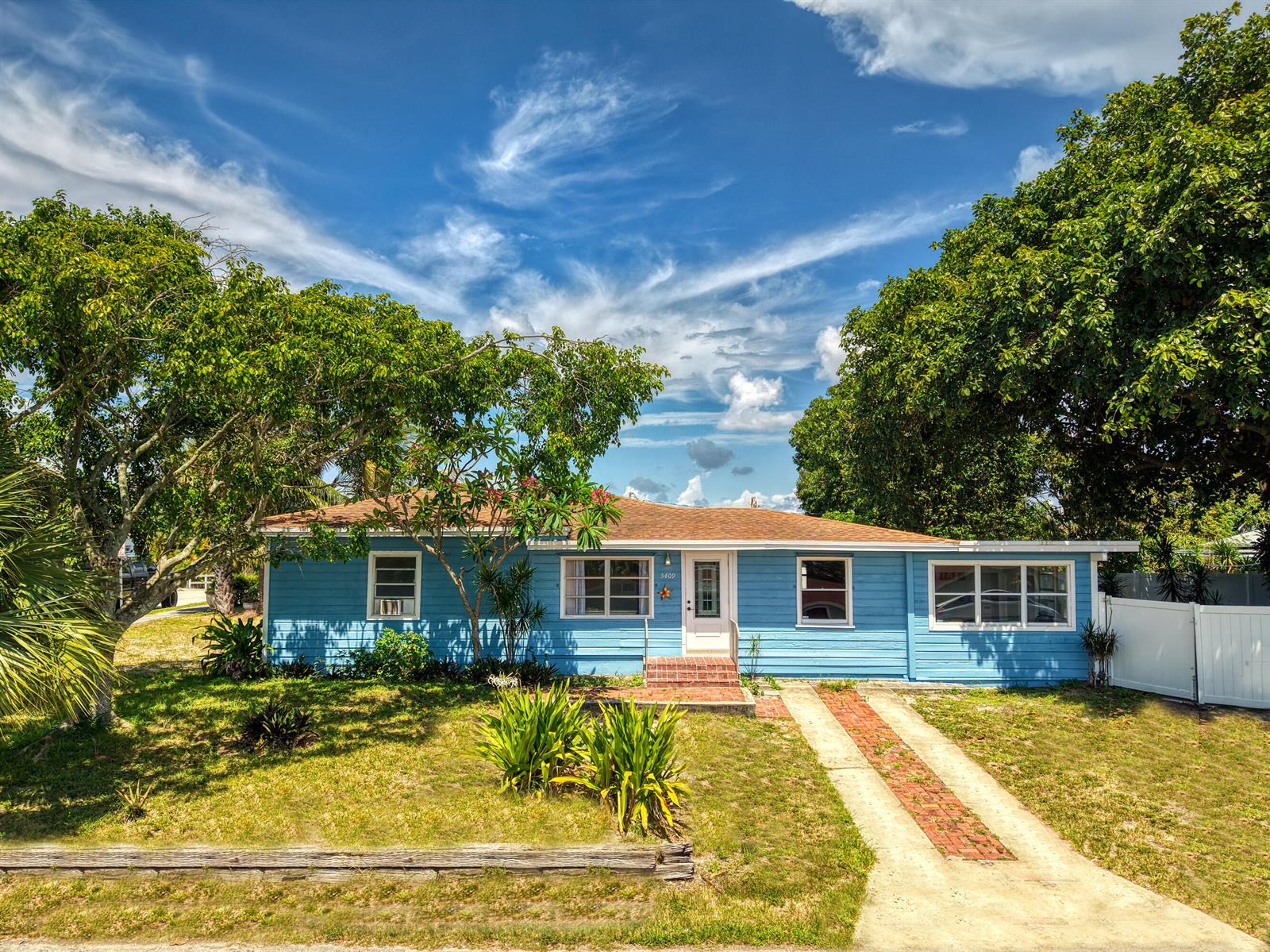 A single-story blue house with a brick driveway and mature trees under a cloudy sky — 5409 Western Avenue, West Palm Beach FL 33405, WEST PALM BEACH, FL