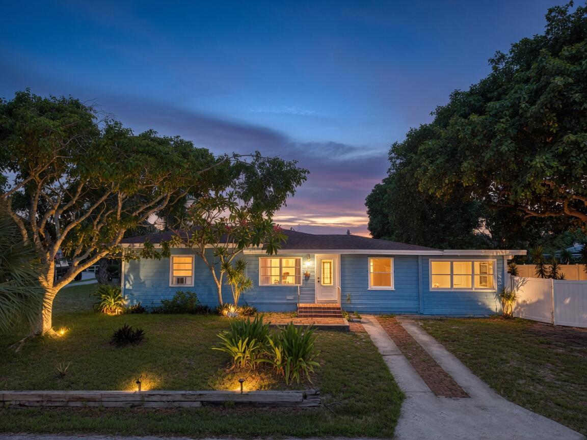 A blue single-story house with a brick driveway and landscape lighting at dusk — 5409 Western Avenue, West Palm Beach FL 33405, WEST PALM BEACH, FL