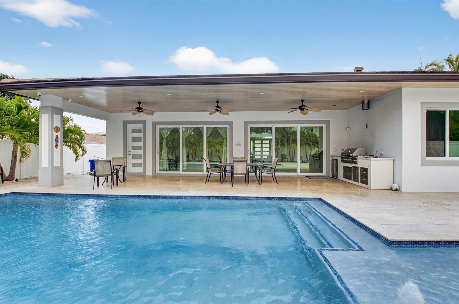 A covered patio with a dining area and outdoor kitchen overlooks a swimming pool — 711 NE 6th Street, Boca Raton FL 33432, BOCA RATON, FL
