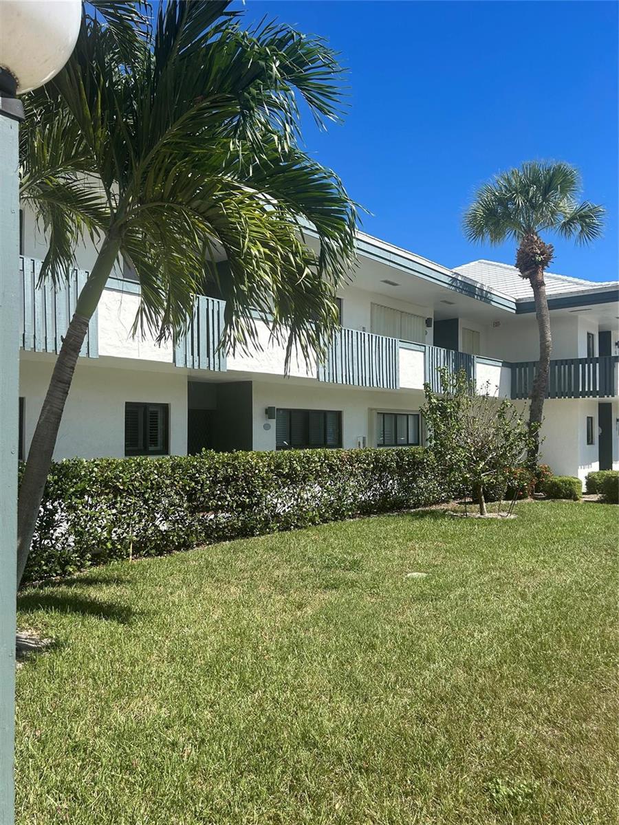 A two-story white apartment building features a green lawn, palm trees, and a hedge — 175 SE Saint Lucie Boulevard # E134, Stuart FL 34996, STUART, FL
