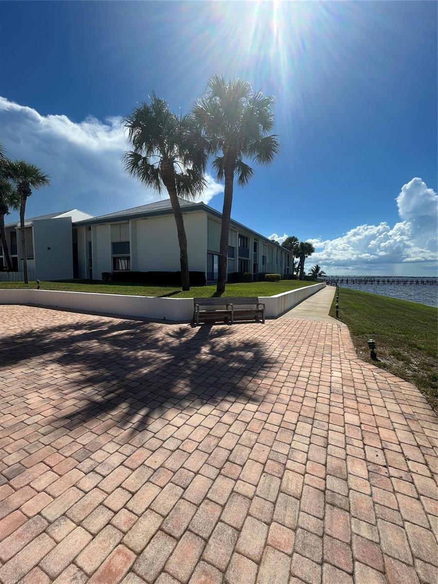 A paved walkway leads past a bench and palm trees toward a waterfront apartment building — 175 SE Saint Lucie Boulevard # E134, Stuart FL 34996, STUART, FL