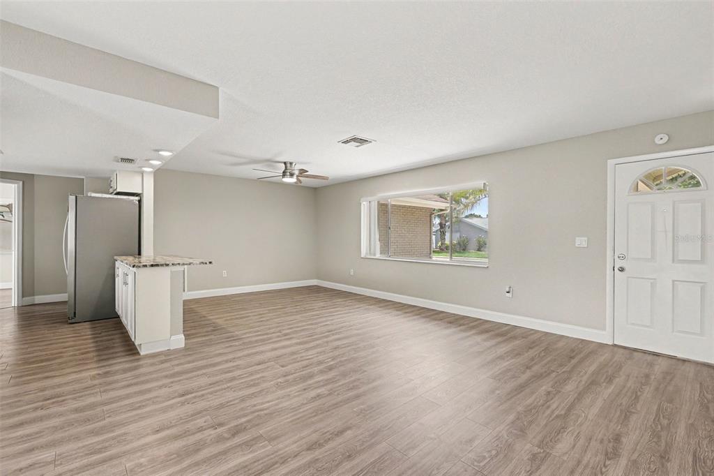 An open-concept living area features light wood-look flooring, a kitchen peninsula, and a front door — 3750 LIGHTHOUSE WAY, HOLIDAY, FL